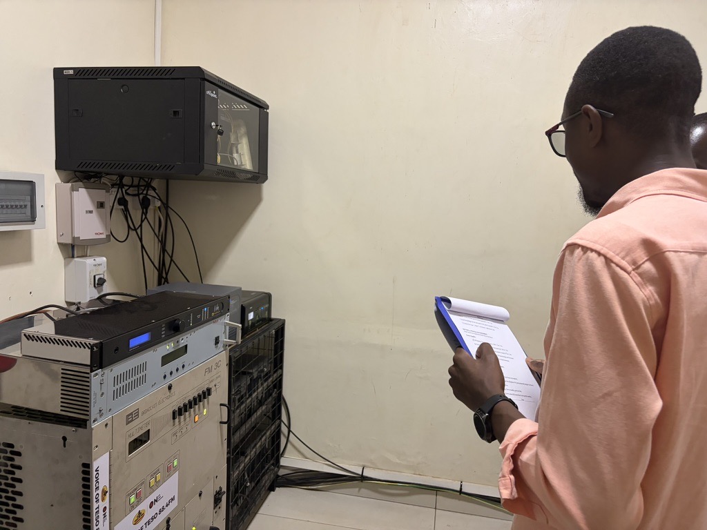 Neuravox team member with a checklist verifying transmitter hardware at radio partner Voice of Teso
